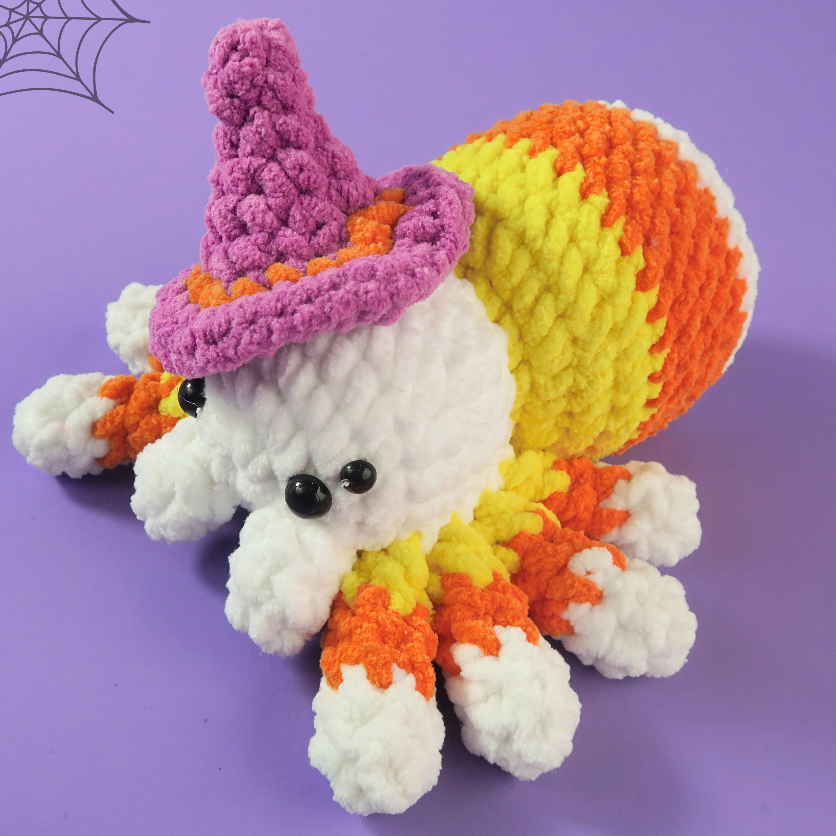 Crocheted Spooky Candy Corn Spider with candy corn pattern and witch hat on a purple background