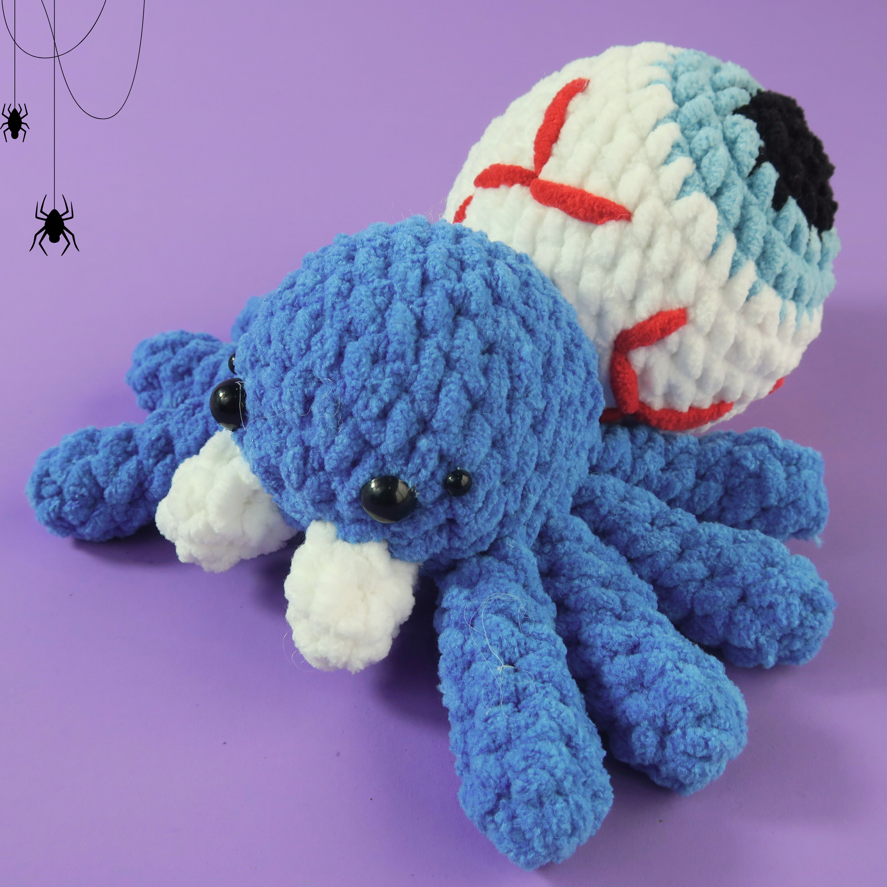 Blue Eyes crochet spider toy with a white and red ball on a purple background