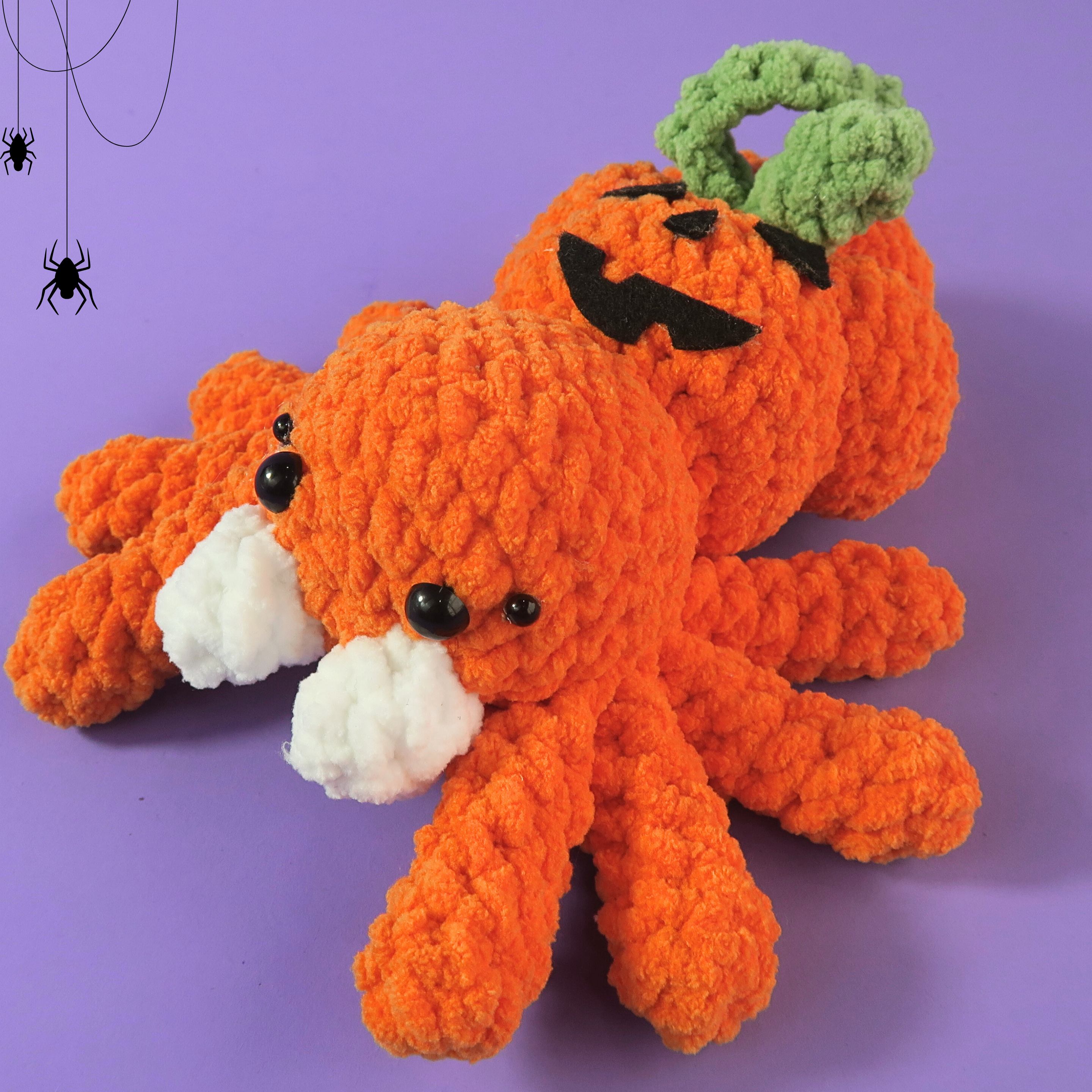 Crocheted orange pumkpin ghost face spider with a pumpkin head on a purple background
