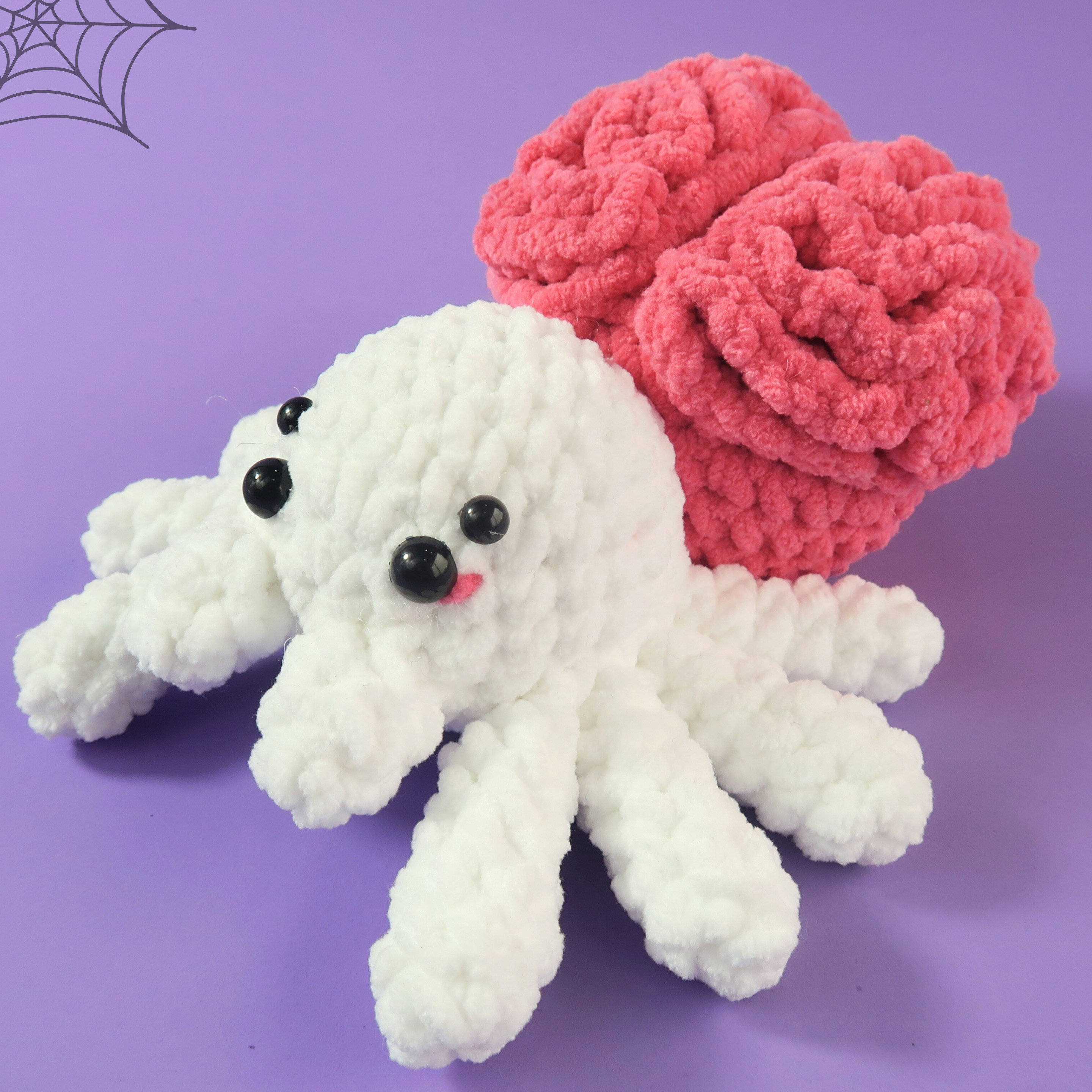 White crocheted spooky spider with a pink brain on a purple background