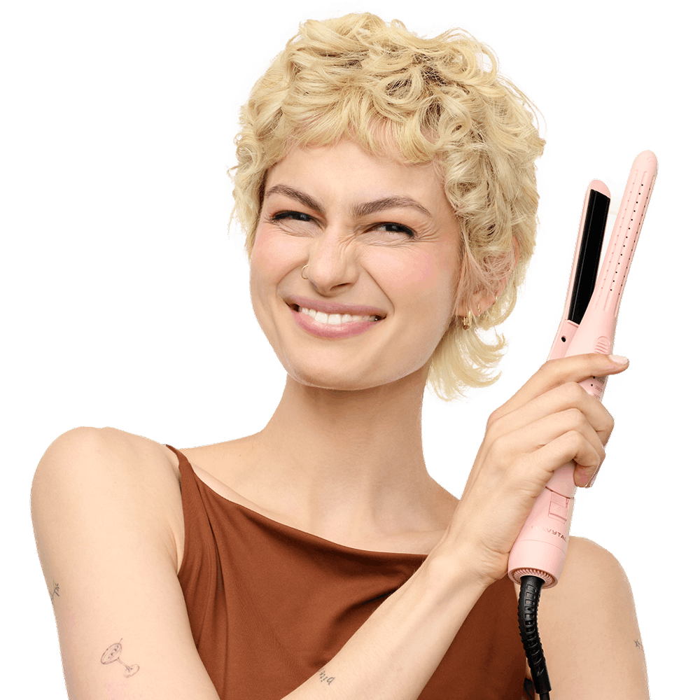 Woman with styled hair holding a pink hair straightener against a black background