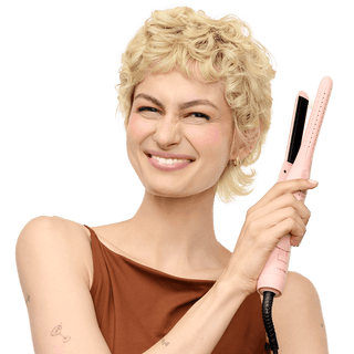 Woman with styled hair holding a pink hair straightener against a black background
