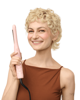 Woman with styled hair holding a pink hair straightener against a black background