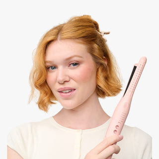 Woman holding a pink hair straightener against a white background
