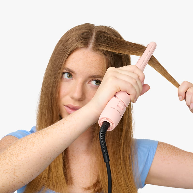 Person using a pink hair straightener on their hair against a white background