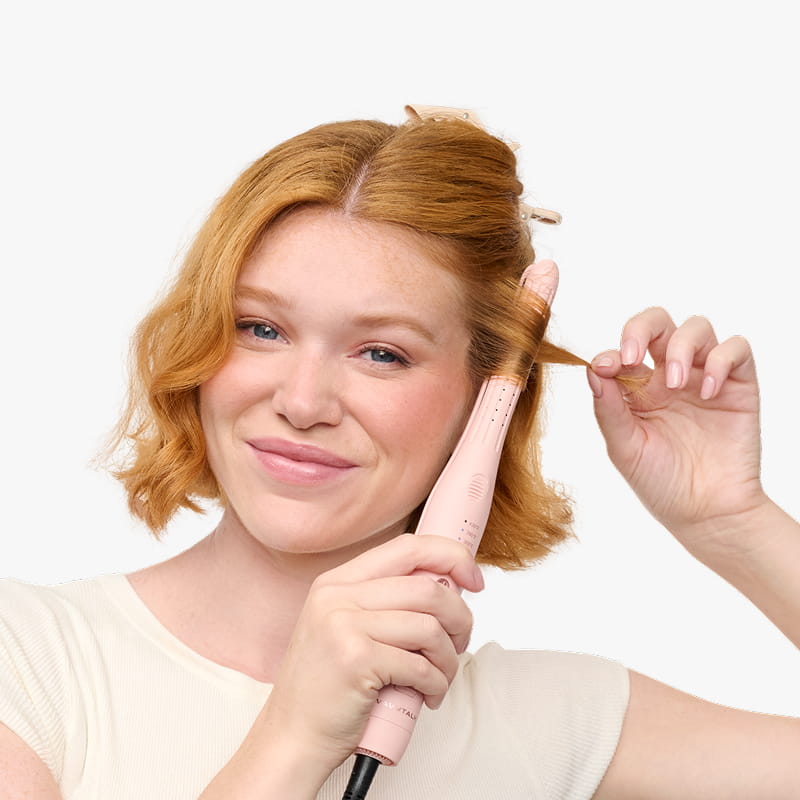Person using a pink hair straightener on their hair against a white background