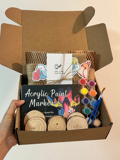 Hand holding an open wooden bird craft kit gift box with acrylic markers, paints and supplies