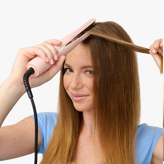 Person using a pink hair straightener on their hair against a white background