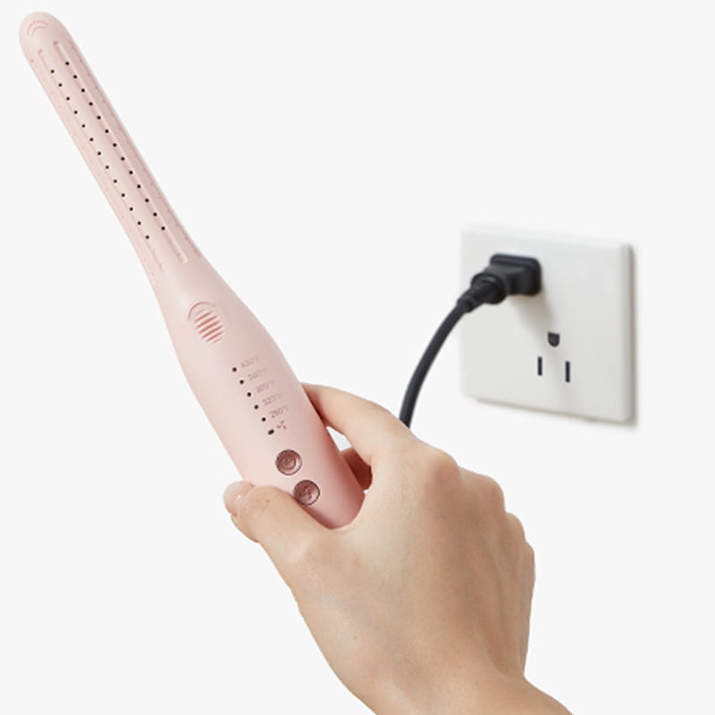 Hand holding a pink hair straightener plugged into an outlet on a white background