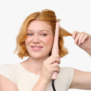 Woman using a pink hair straightener on her hair against a white background