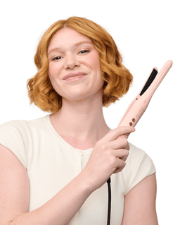 Woman with red hair holding a pink hair straightener against a black background