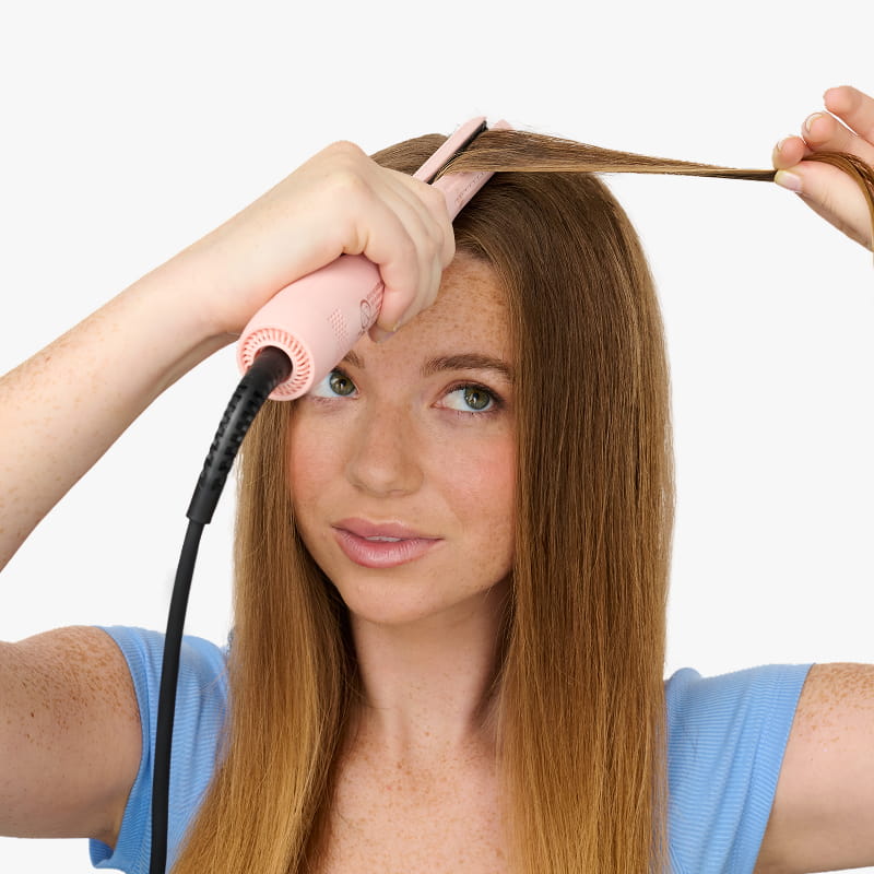 Woman using a hair straightener on her hair against a white background