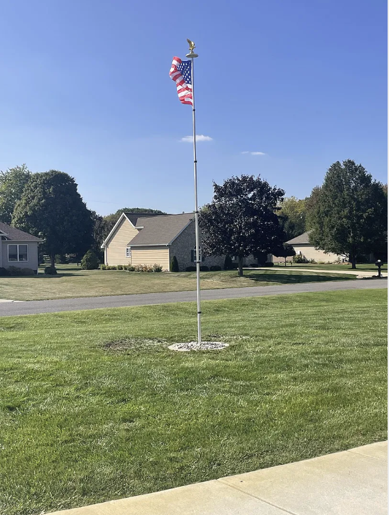 American flag on a flagpole in a residential area with houses and trees in the background.