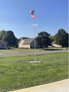 American flag on a flagpole in a residential area with houses and trees in the background.