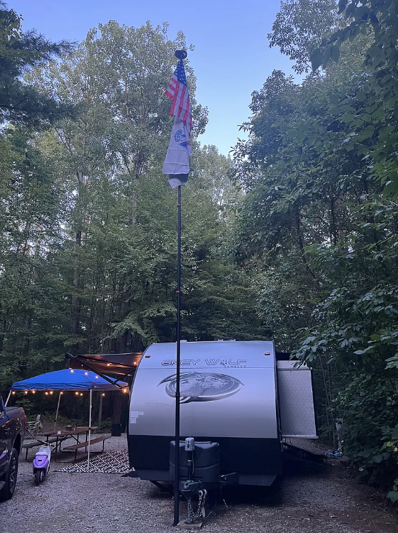 Small trailer parked in a wooded area with an American flag on a pole.