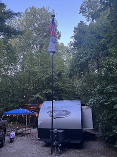 Small trailer parked in a wooded area with an American flag on a pole.